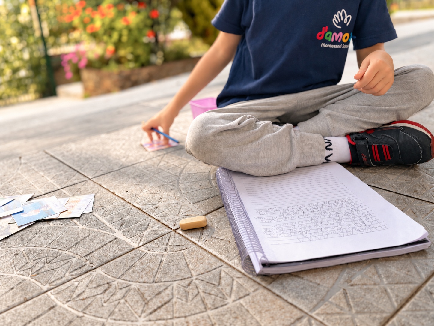Alumno trabajando con tarjetas y un cuaderno en el patio de D’amore, sin mostrar su rostro