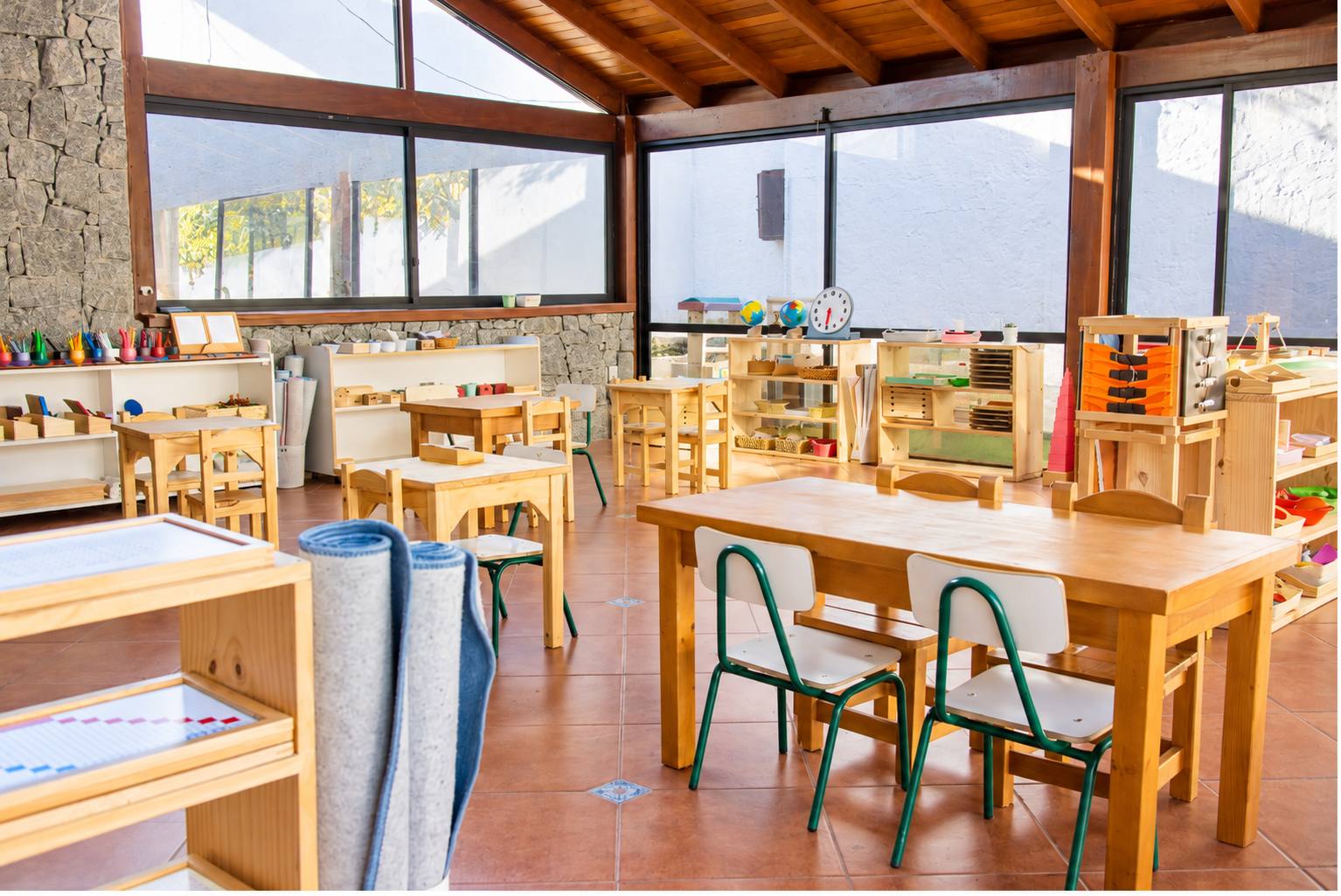 Ambiente de Children’s House con mesas pequeñas y estantes de materiales Montessori