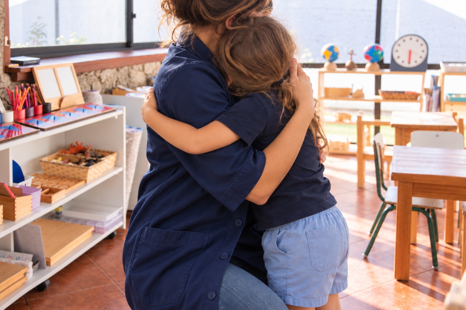Docente con túnica azul marino abrazando a una niña en el ambiente, sin rostros visibles