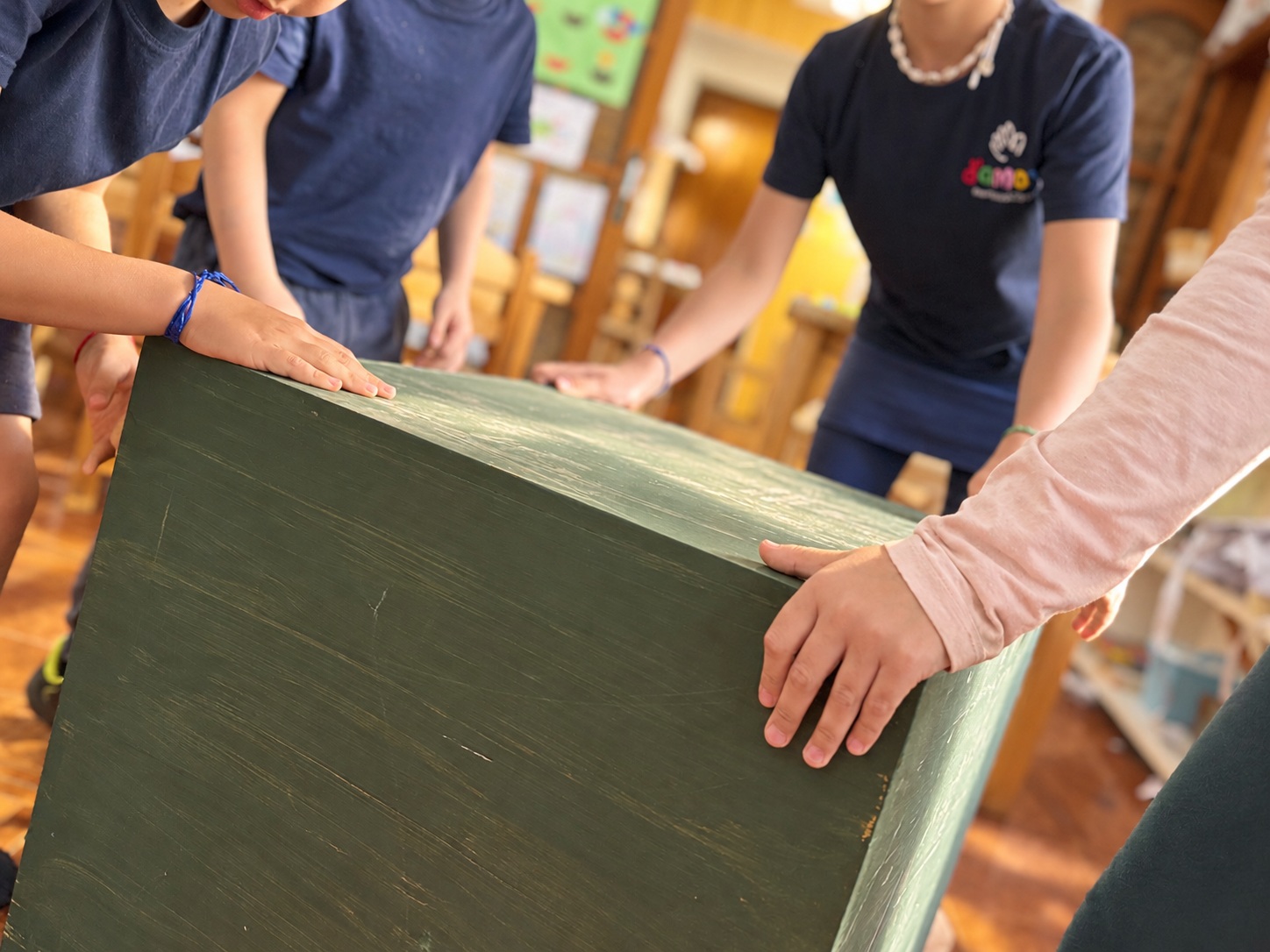 Manos colaborando sobre una pieza de madera en el colegio