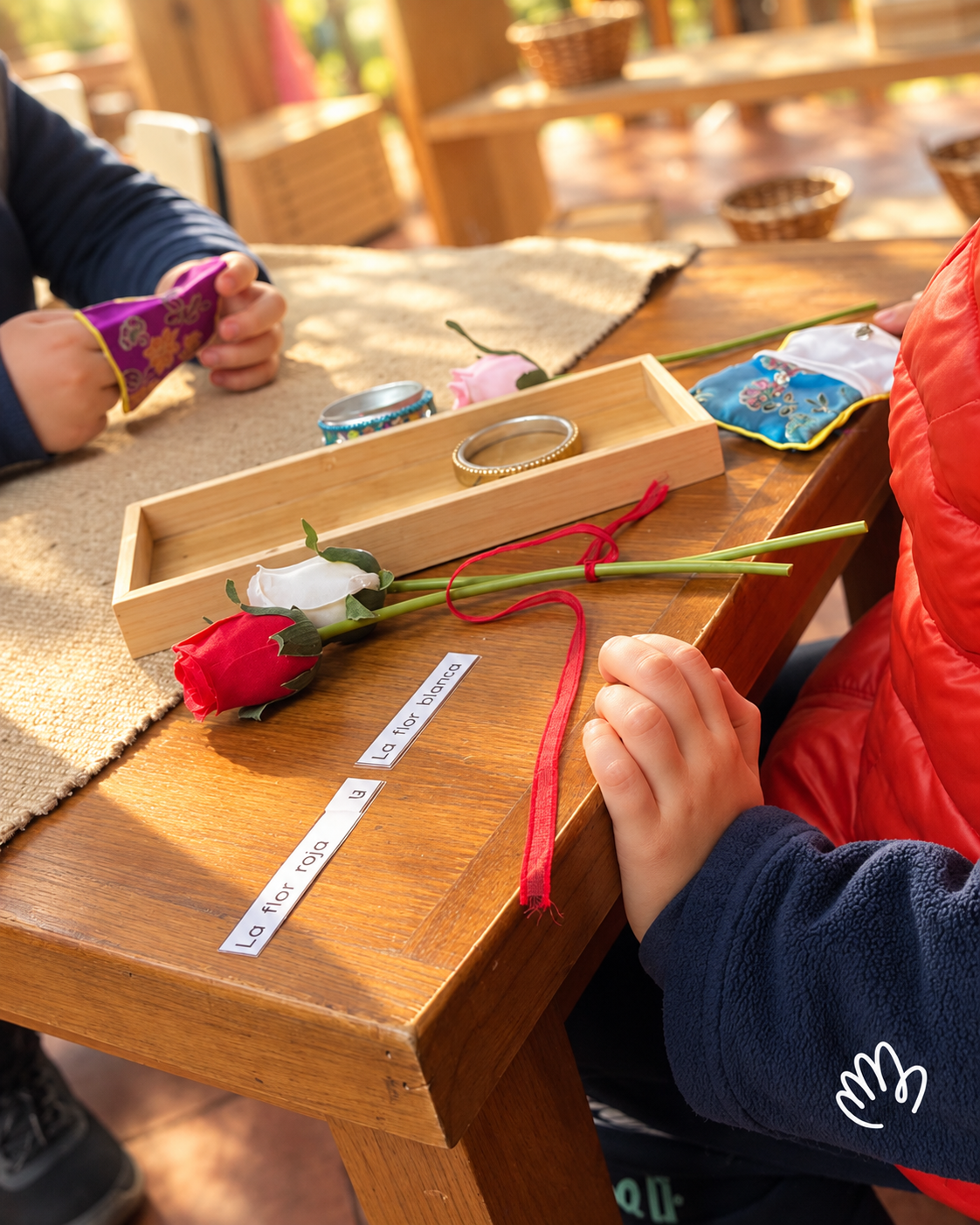 Manos trabajando con flores, tarjetas de lectura y objetos en un ambiente de D’amore