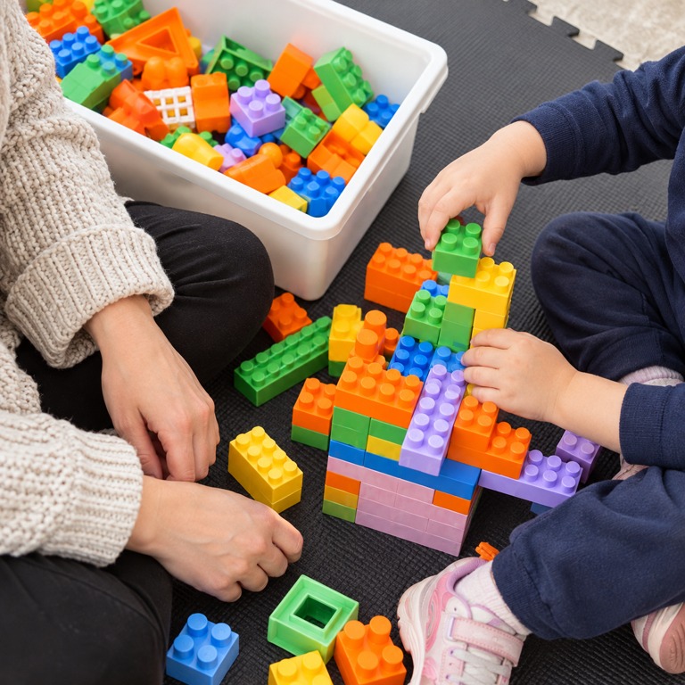Niño jugando con bloques junto a una persona adulta, sin rostros visibles