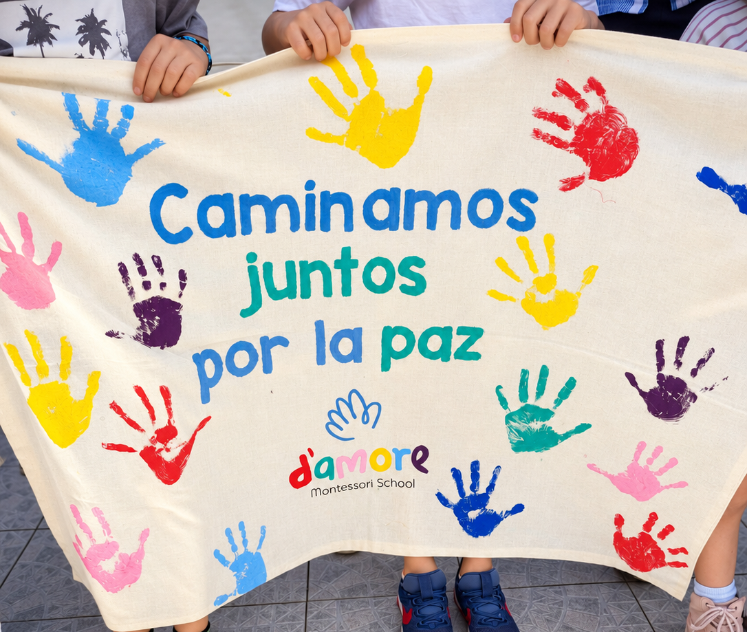 Niños sosteniendo un cartel de D’amore que dice Caminamos juntos por la paz, decorado con huellas de manos de colores